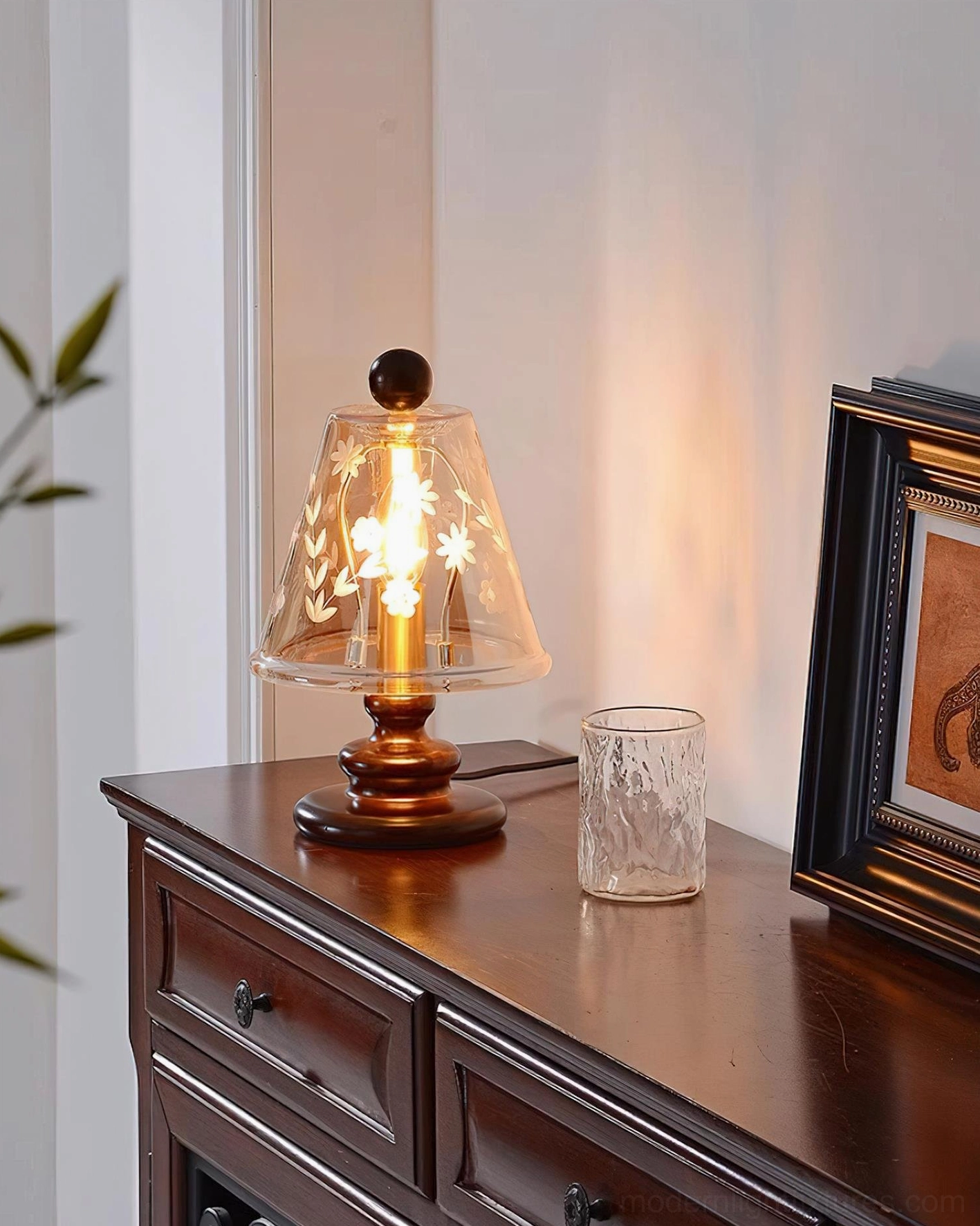 Lit Tilda table lamp with warm cognac glass shade on bedroom dresser, side three-quarter view showing floral etch details