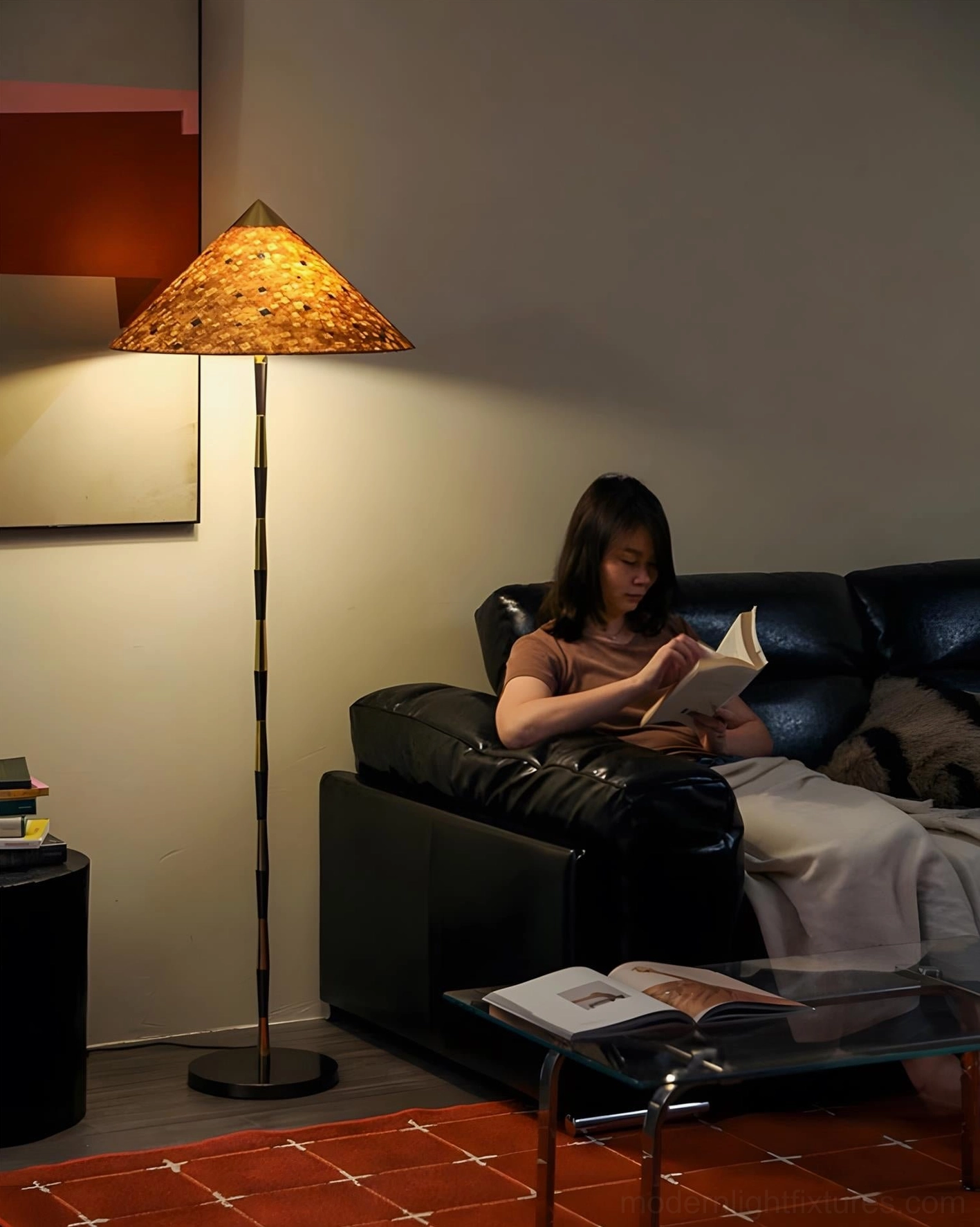 Timbre floor lamp beside leather sofa in living room with red area rug, woman reading by warm light