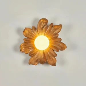 Natural wood Tina flower wall lamp mounted on light gray wall, matte petal frame with warm glowing light center