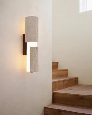 Tolira wall sconce installed in residential stairwell, side perspective showing warm ambient lighting and natural texture of travertine stone