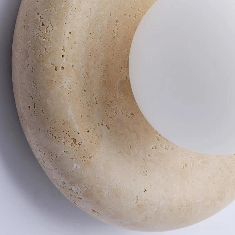 Close-up detail of yellow travertine disc with natural veining and pitting on orb wall sconce