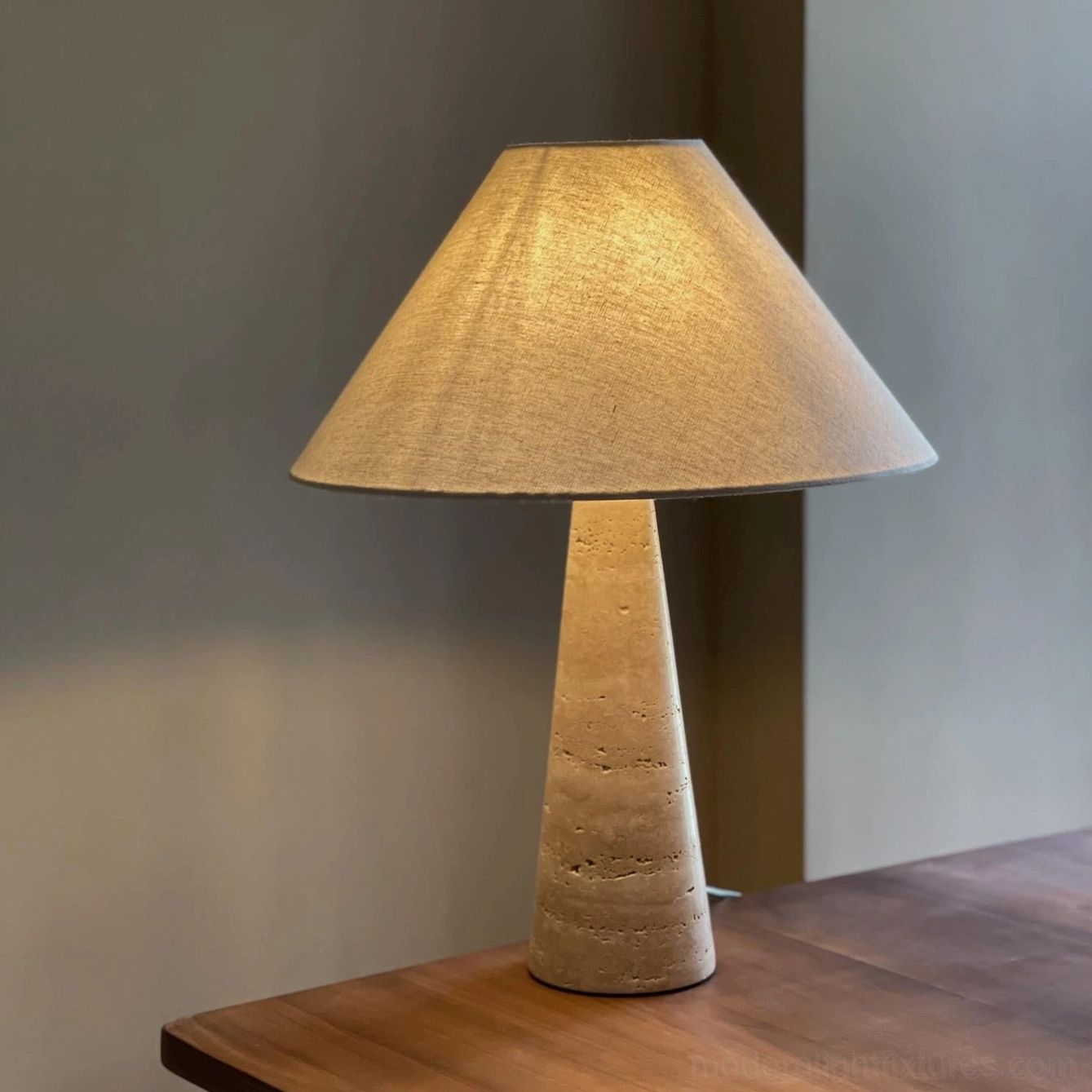 Lulu travertine lamp illuminated with warm ambient lighting and linen shade against gray wall in minimalist interior