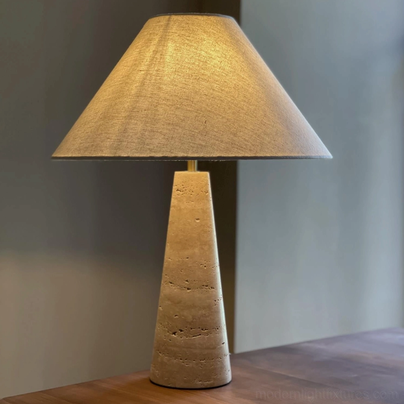 Natural travertine stone table lamp in beige with hand-finished conical base on wooden table surface showing authentic mineral texture
