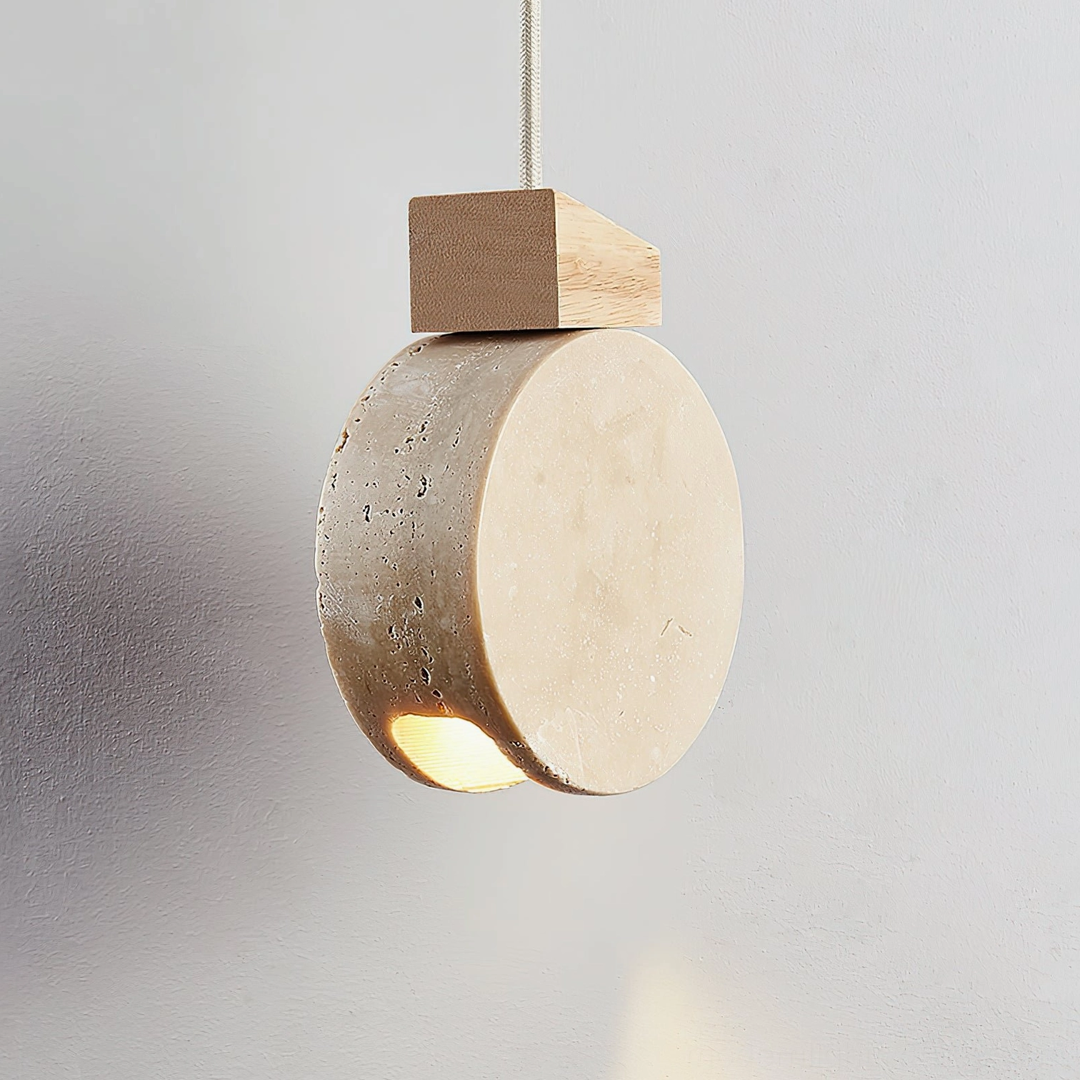 Travertine stone pendant light left three-quarter view showing natural pores and warm suspended lighting effect