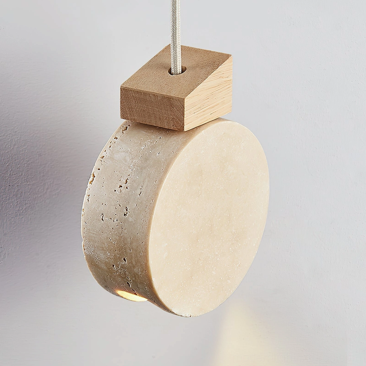 Close-up right view of travertine disc pendant light showing light wood top cap and detailed stone texture
