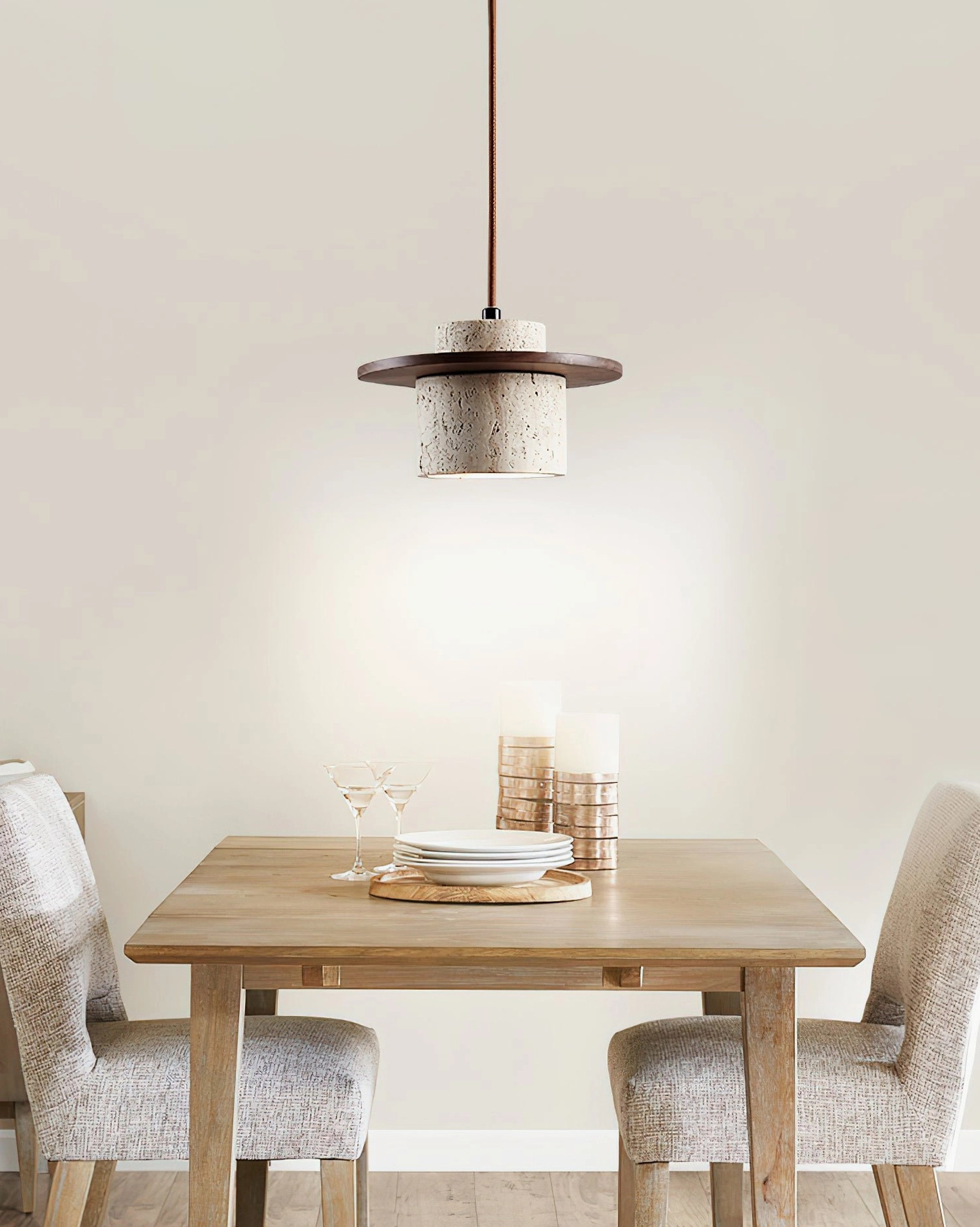Travertine stone hanging pendant light in farmhouse dining room, warm illuminated glow over wooden table with neutral decor