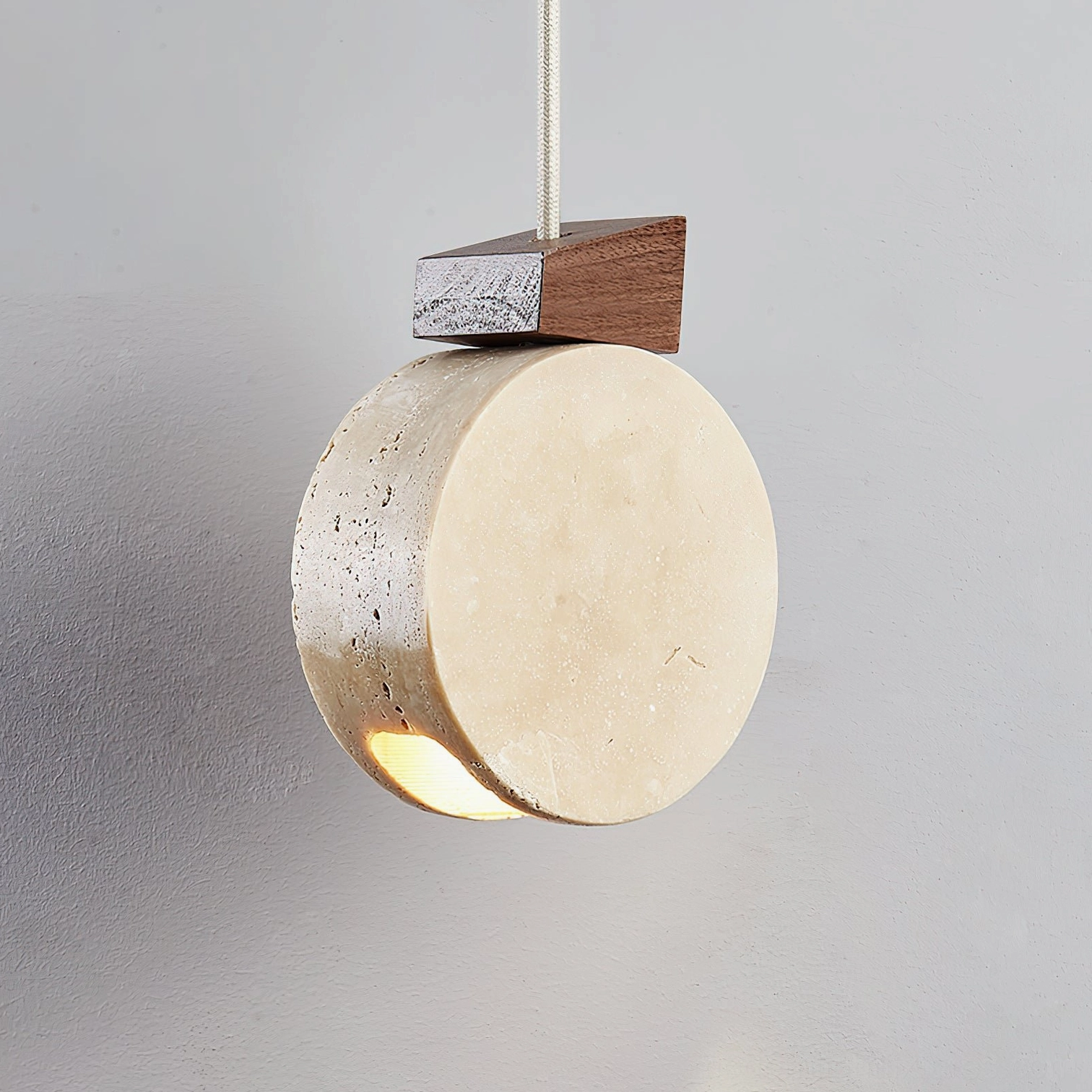 Natural travertine disc pendant lamp illuminated three-quarter view showing warm downlight glow and stone texture