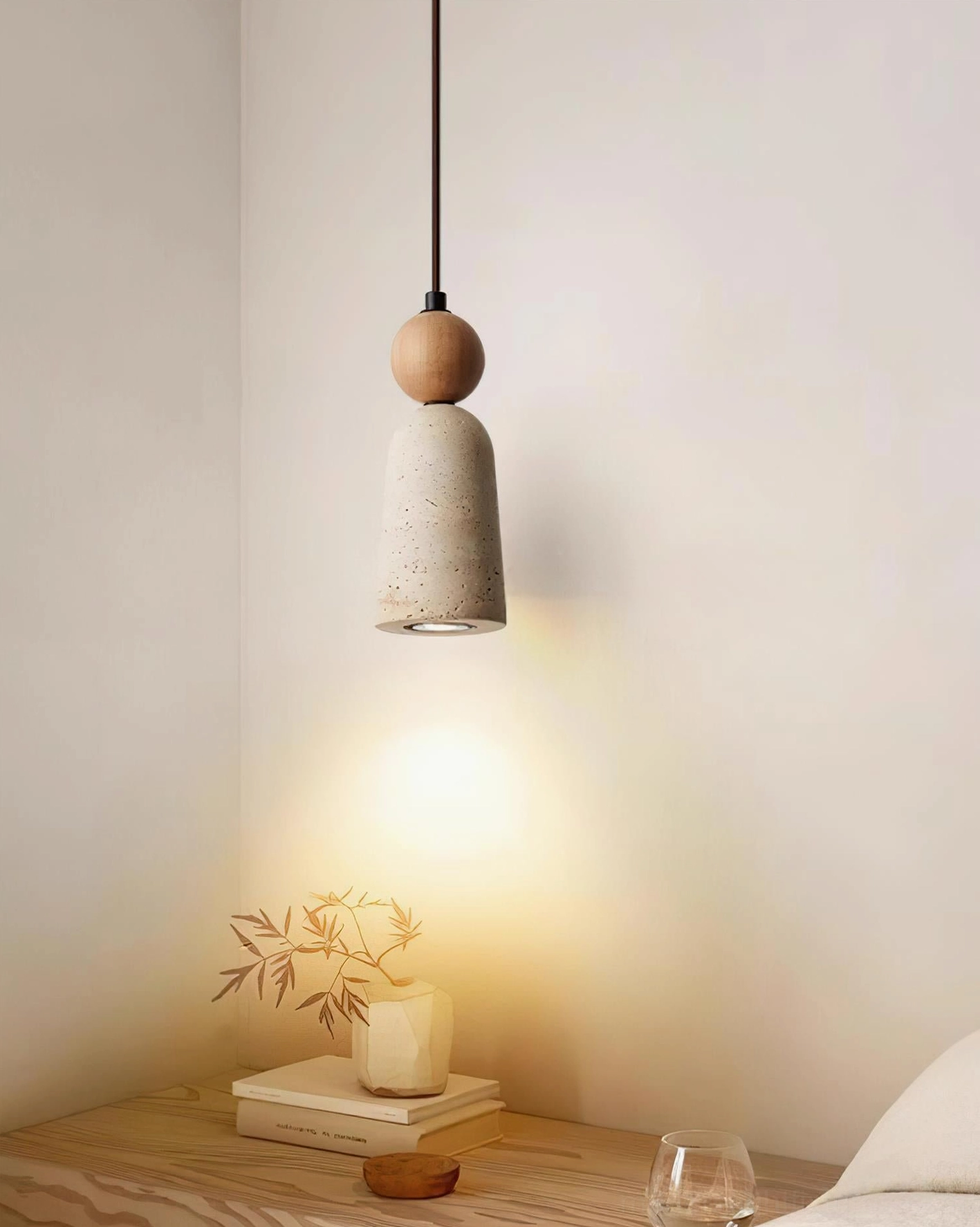Minimalist bedroom corner with Bellin travertine pendant light, books, and potted plants on nightstand