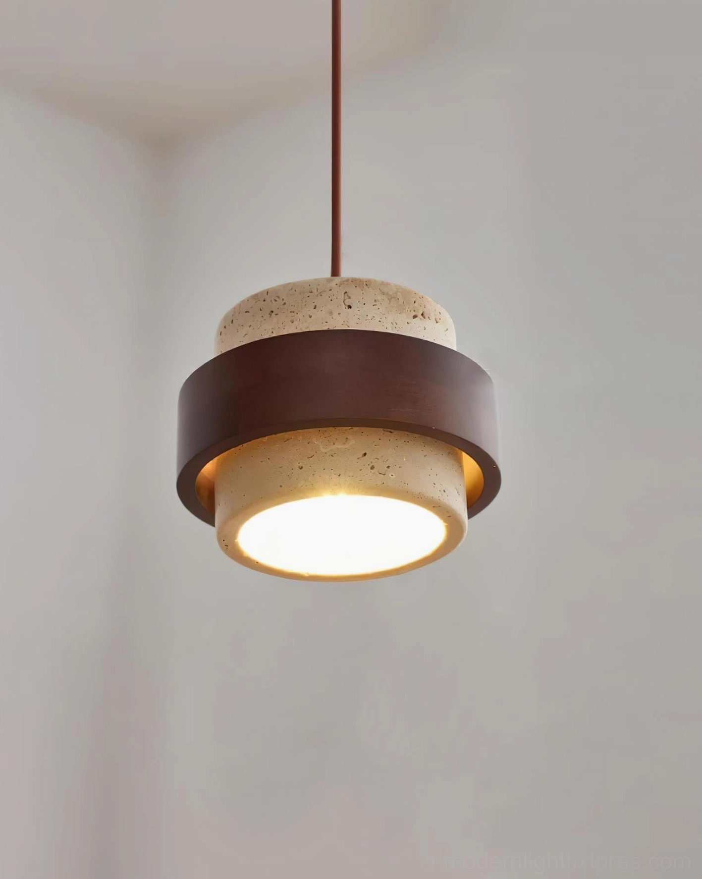 Stone pendant light three-quarter angle view with illuminated warm glow, brown suspension cord visible, showing sculptural form
