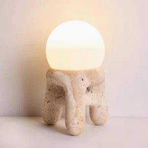 Lit travertine table lamp with warm ambient glow, front three-quarter view against neutral wall