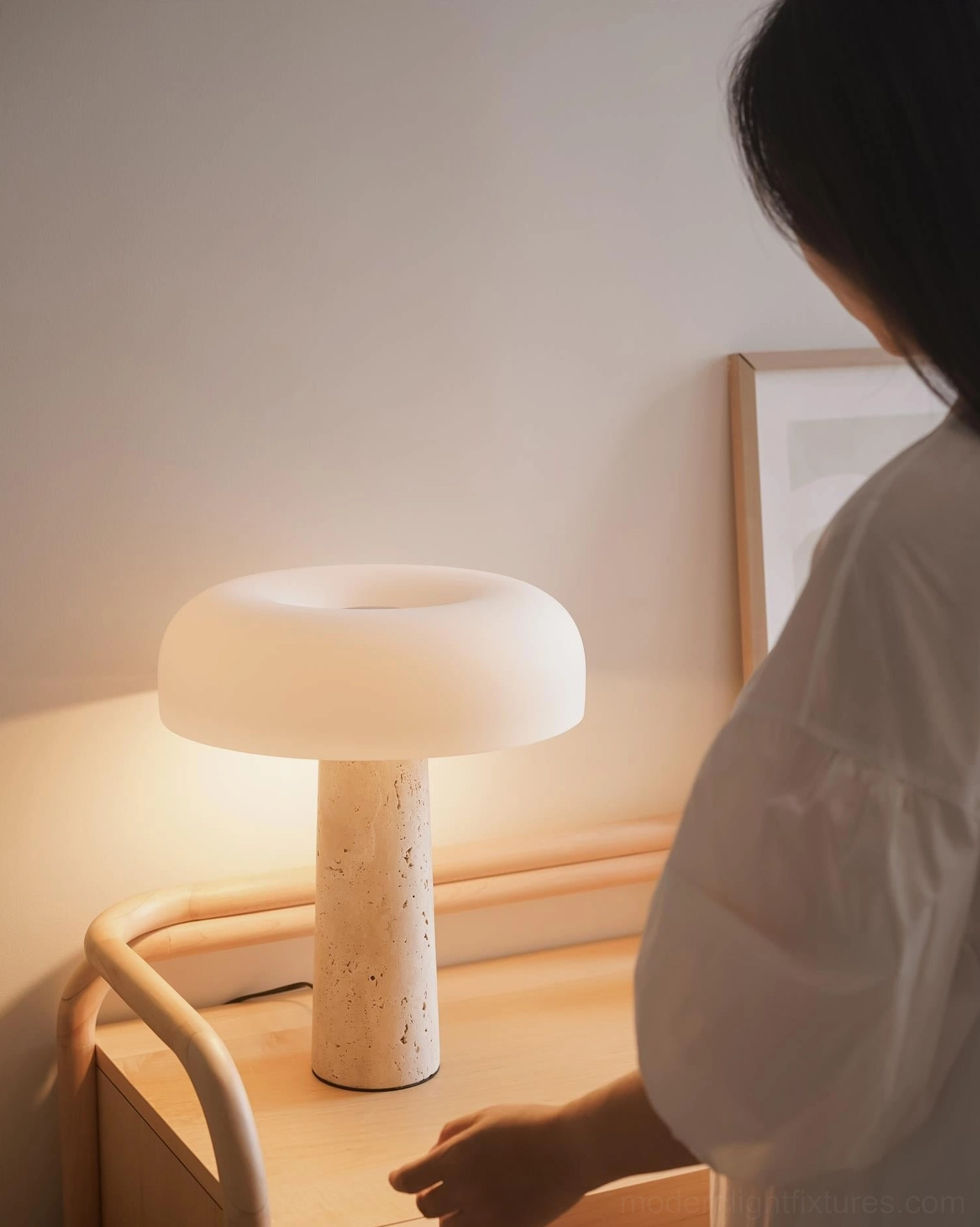 Travertine table lamp on wooden bedroom nightstand, glowing warm light in cozy minimalist bedroom setting