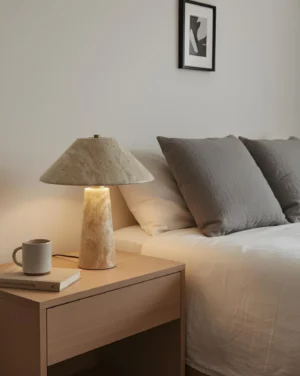 Travertine bedside lamp positioned on modern light wood nightstand next to grey linen bedding in contemporary bedroom