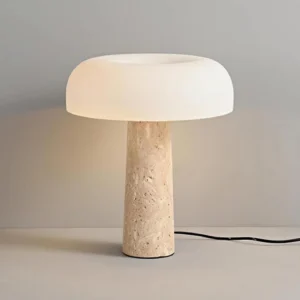 Lit travertine table lamp in studio setting, three-quarter angle displaying warm white LED light diffusion through glass shade
