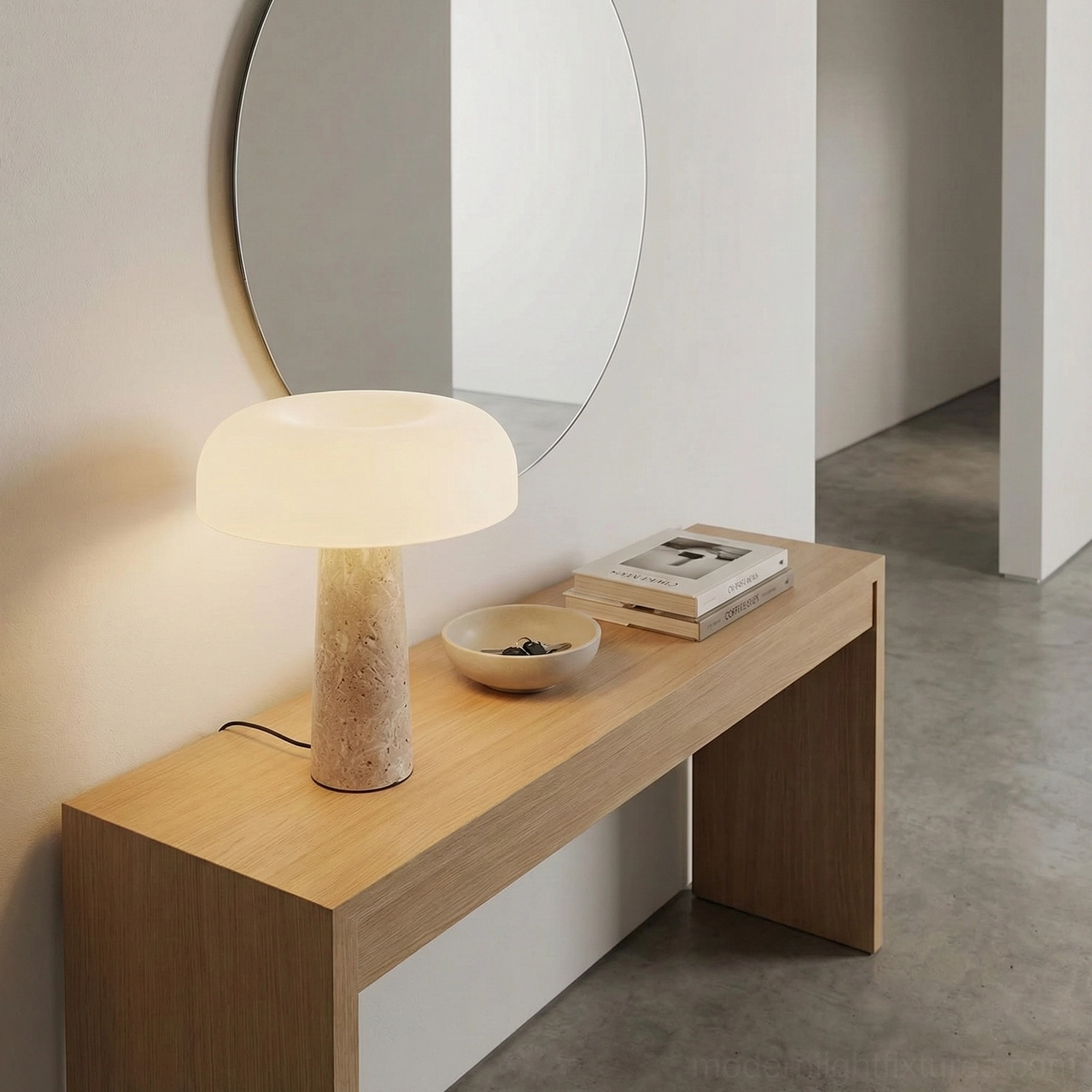 Travertine stone table lamp positioned under round wall mirror in minimalist vanity area with books and decor