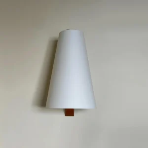 Trianora modern minimalist wall lamp mounted on warm interior wall with tall tapered white shade and compact wood base