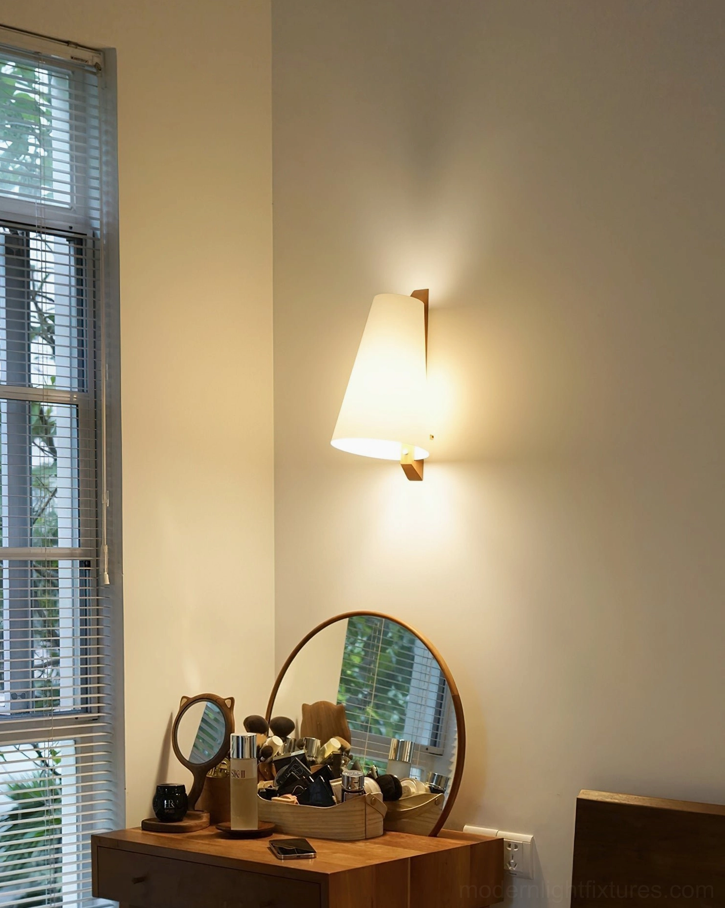 Lit Trianora wall sconce creating soft warm glow in cozy bedroom vanity setting with minimalist décor