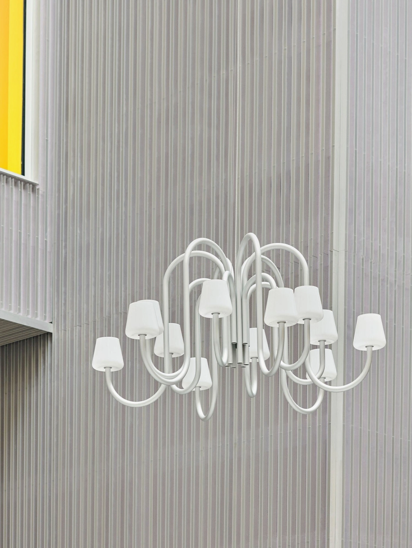 Trilo chandelier with white metal frame and tapered white glass shades against vertical ribbed wall