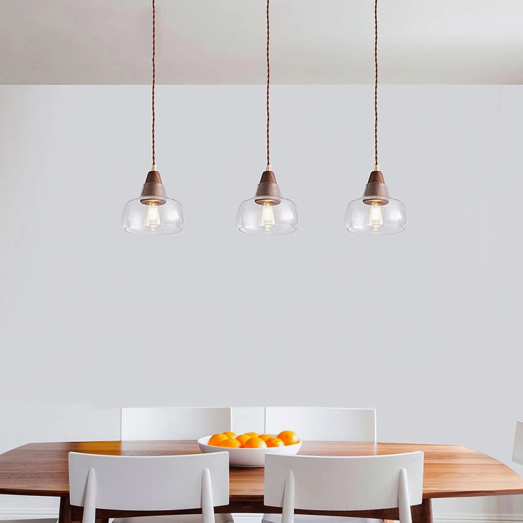 Triple walnut glass pendant lights synchronized above wooden dining table in minimalist space, contemporary fixture arrangement
