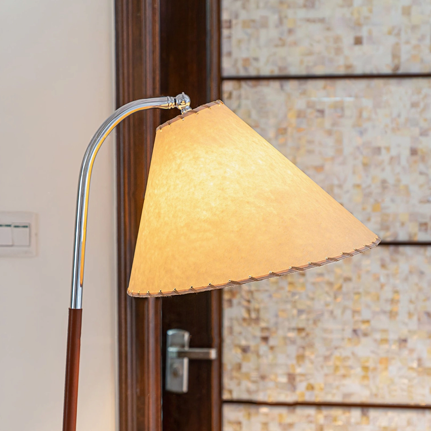 Close-up detail of tripod floor lamp components showing linen fabric shade, chrome curved metal arm, and lamp construction against tiled accent wall