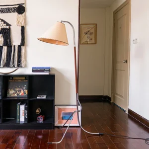 Tripod floor lamp in vintage hallway setting with bookshelf, walnut finish pole paired with chrome metal tripod base, fabric shade providing warm ambient lighting