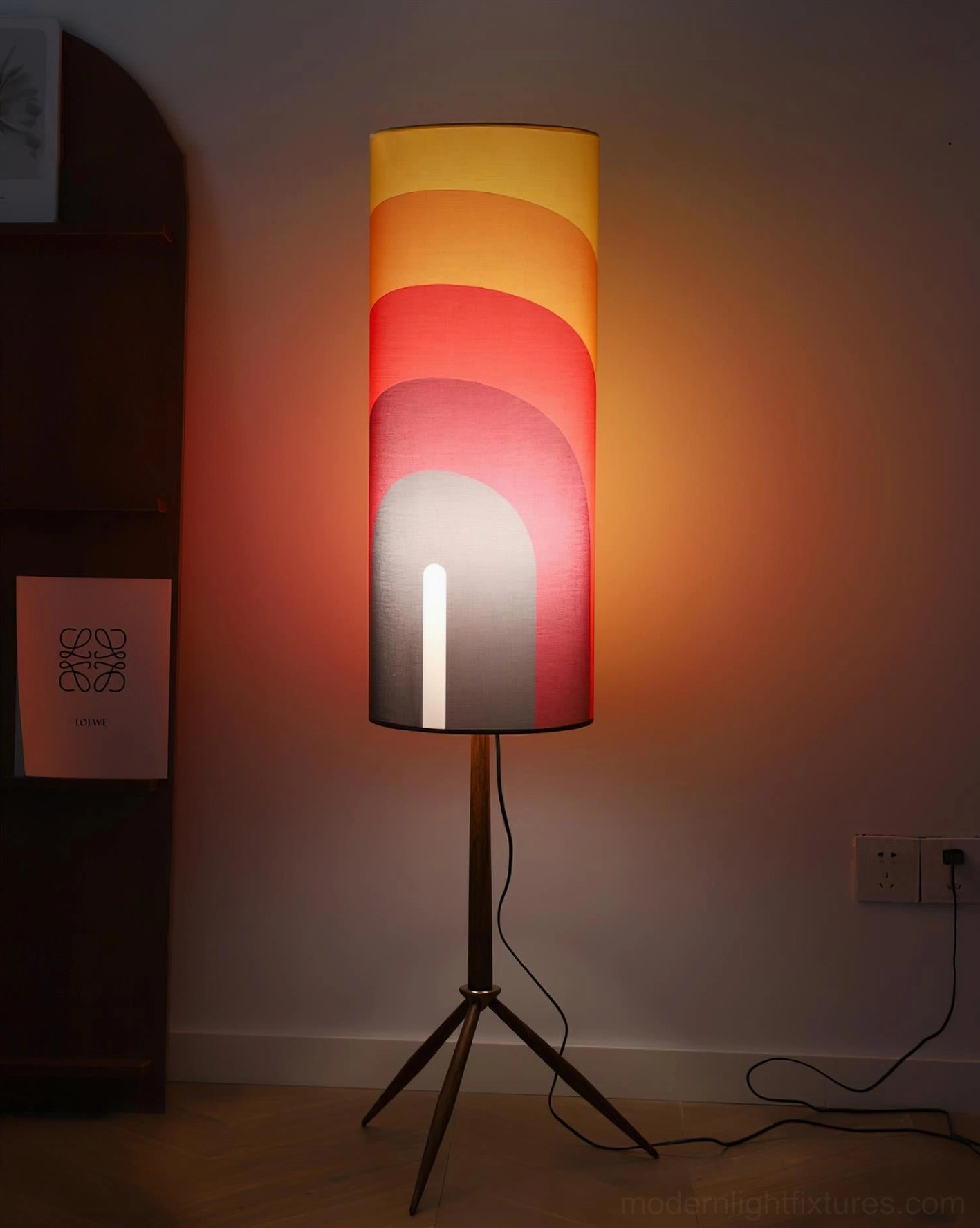 Illuminated mid-century tripod floor lamp glowing in dimly lit home room, showcasing warm ambient light from gradient fabric shade