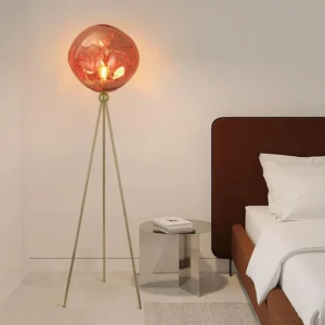 Contemporary tripod floor lamp with brass gold stand and round red glass shade positioned in modern master bedroom