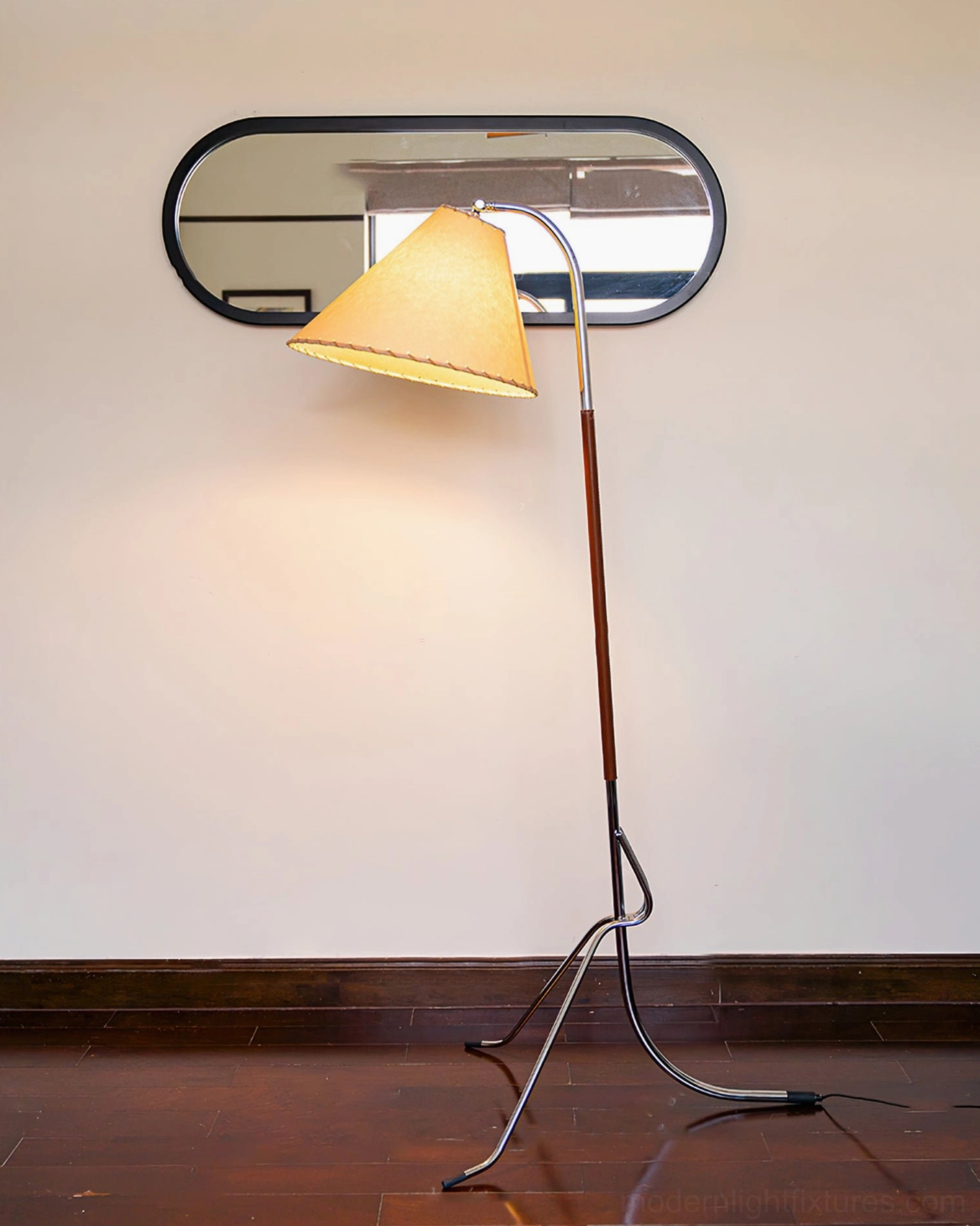 Tripod floor lamp side rear three-quarter view against residential wall with oval mirror, metal tripod base and solid wood lamp pole construction