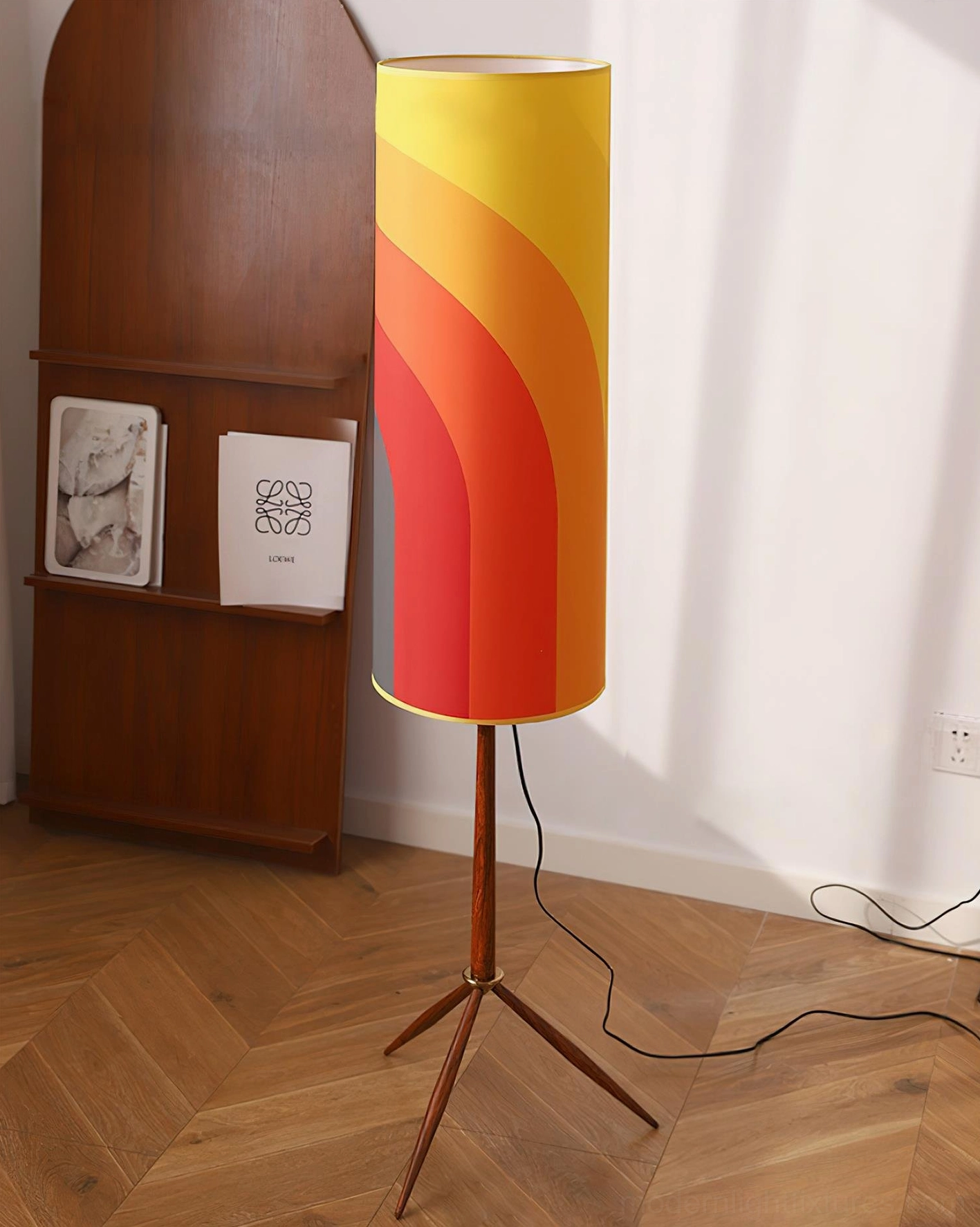 Warm gradient tripod floor lamp in herringbone wood floor living space beside wooden bookshelf with wall art display