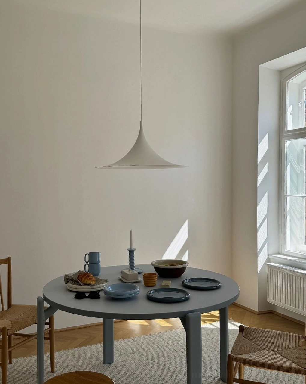 White trumpet pendant light in small modern dining nook with gray round table sunlight