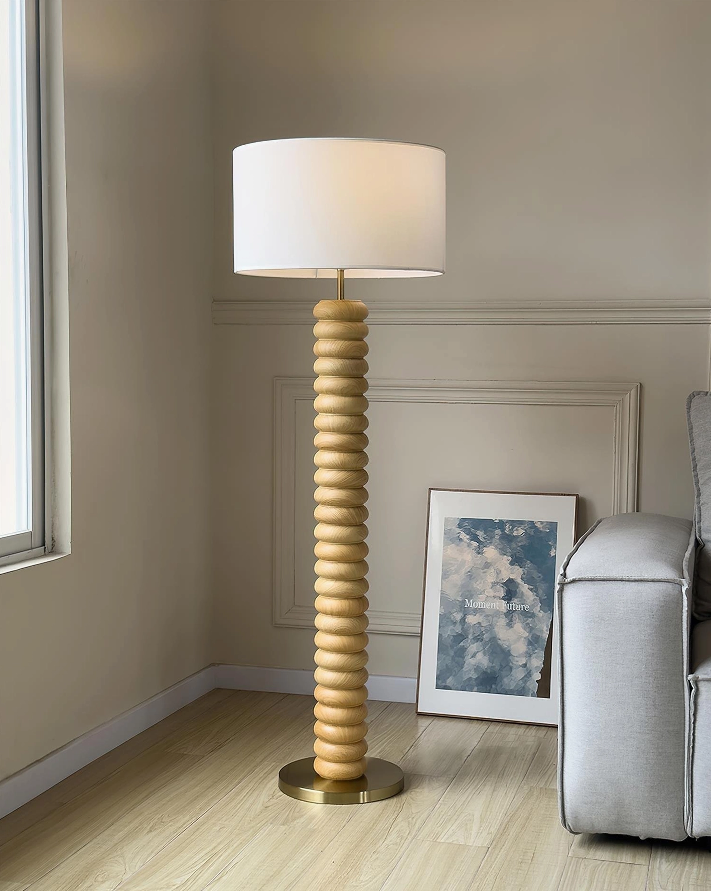 Light natural wood spiral floor lamp with brass base and white fabric shade in minimalist living room with grey sofa
