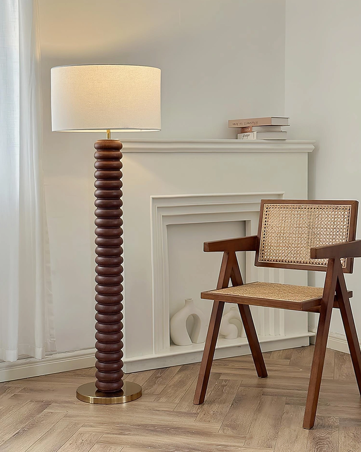 Dark brown walnut ribbed wooden modern floor lamp with brass base and beige lampshade near fireplace and rattan furniture