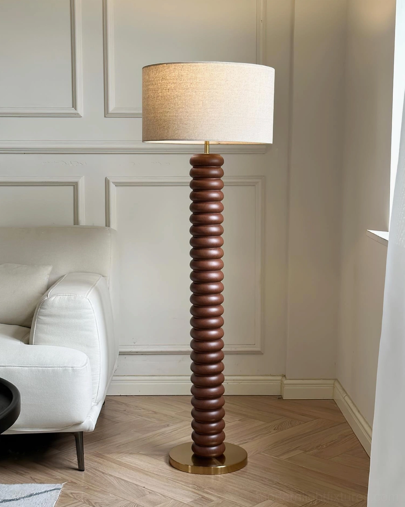 Dark walnut wood spiral ribbed floor lamp with brass base and beige fabric shade beside white upholstered sofa
