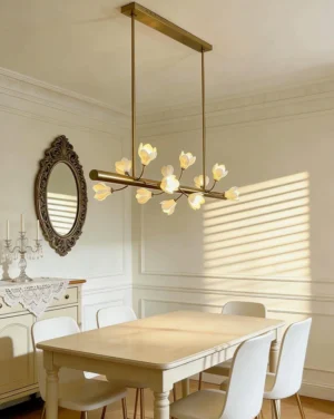 Tuloria brass chandelier illuminated over modern dining table with white place settings and wall mirror