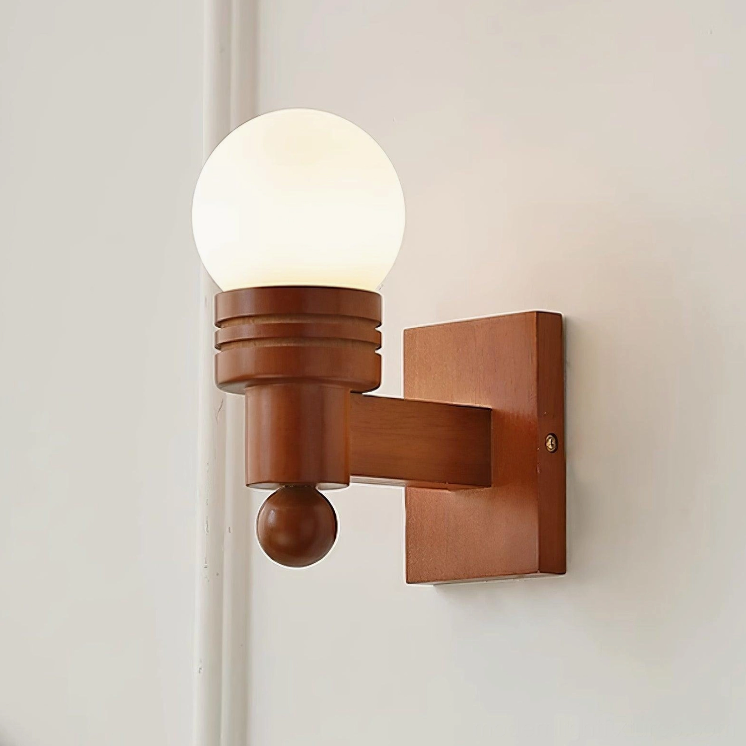 Walnut wood and frosted white glass wall sconce mounted on white interior wall, close-up detail of spherical shade design
