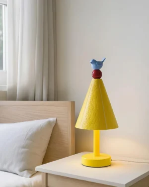 Ceramic bird table lamp positioned on light wood nightstand in warm bedroom setting with soft lighting