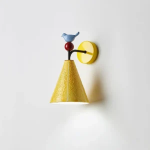 Modern yellow ceramic wall sconce with bird detail emitting warm downlight, side angle showing light distribution