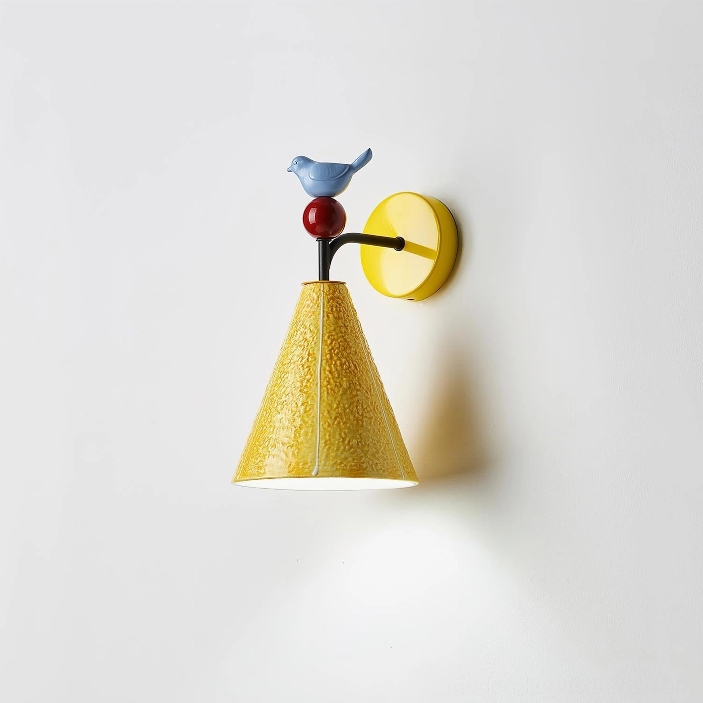 Modern yellow ceramic wall sconce with bird detail emitting warm downlight, side angle showing light distribution
