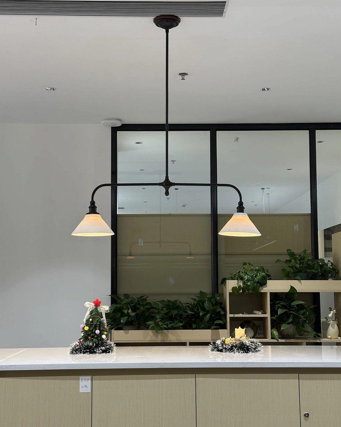 Two-light brass linear chandelier with white conical ceramic shades suspended in bright transitional kitchen space