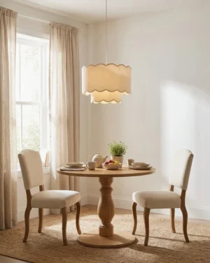 Two-tier scalloped pendant light hung above round wooden dining table in warm neutral dining room with beige layered drum shade
