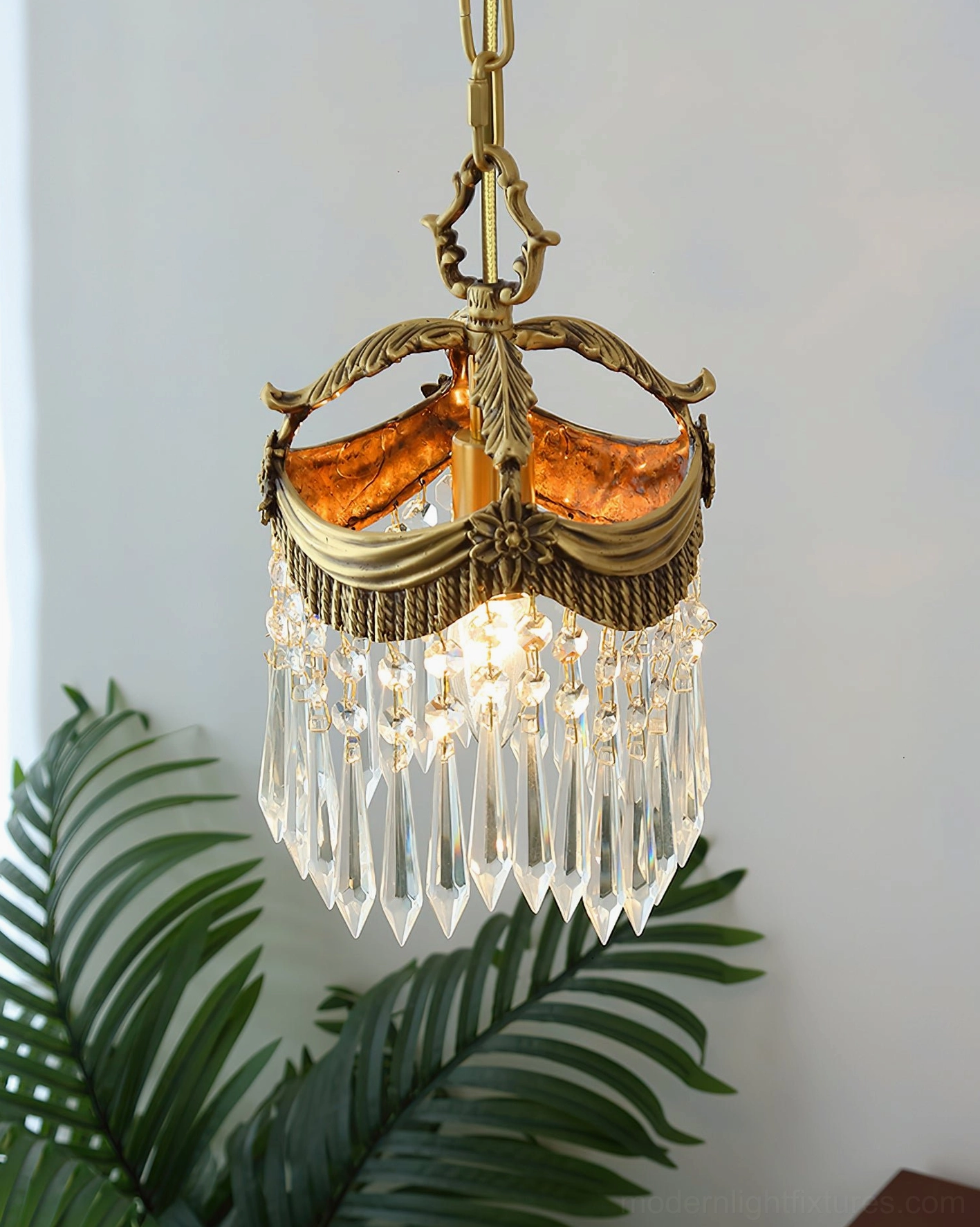 Vacarro pendant light hanging in botanical interior setting with brass frame and crystal shade