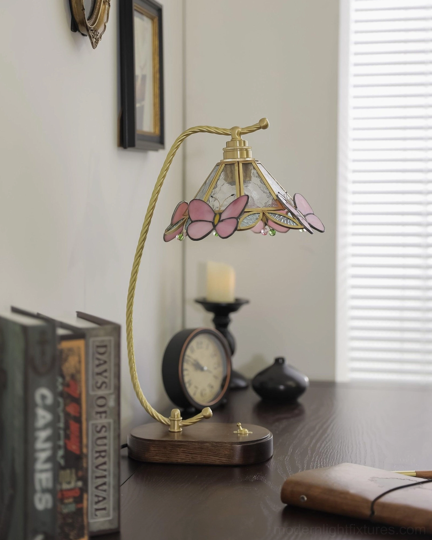 Valerie Butterfly decorative table lamp on retro vintage desk with books and clock, showing brass arm and light purple-pink butterfly decorative elements