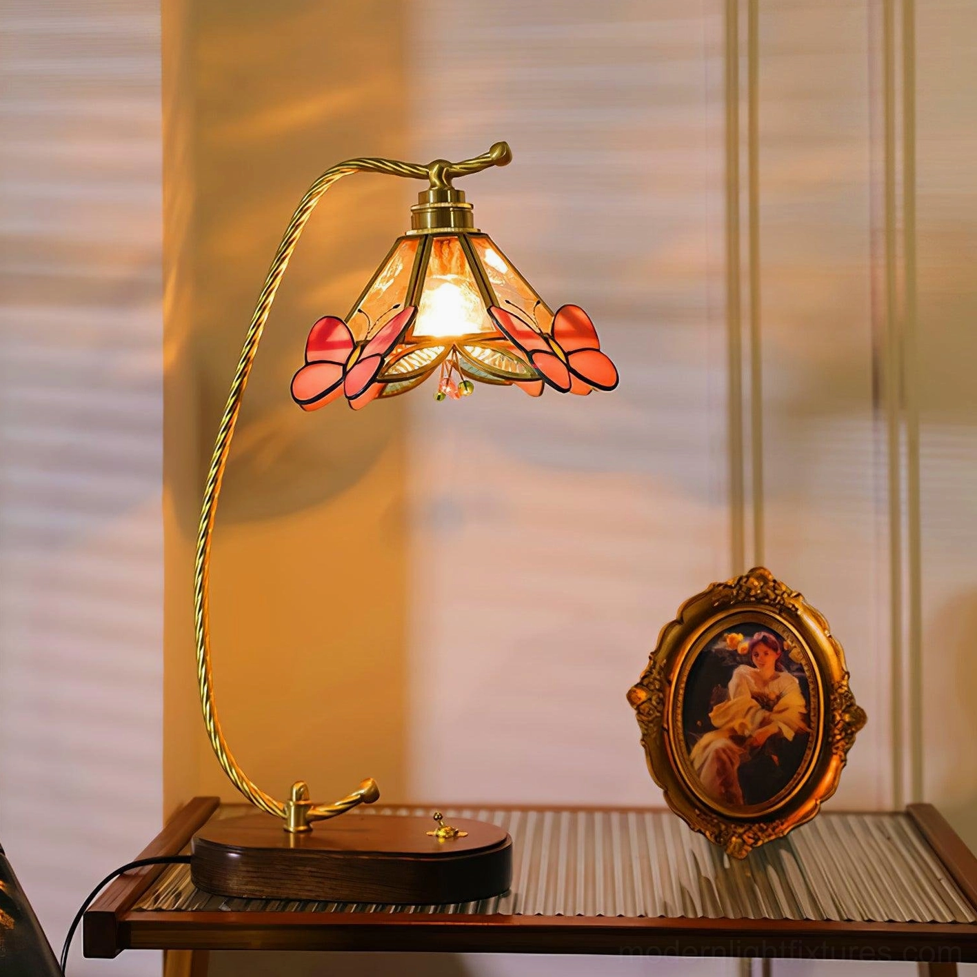Side profile of Valerie Butterfly table lamp on desk with vintage portrait frame, showing warm glowing light and pastoral vintage aesthetic