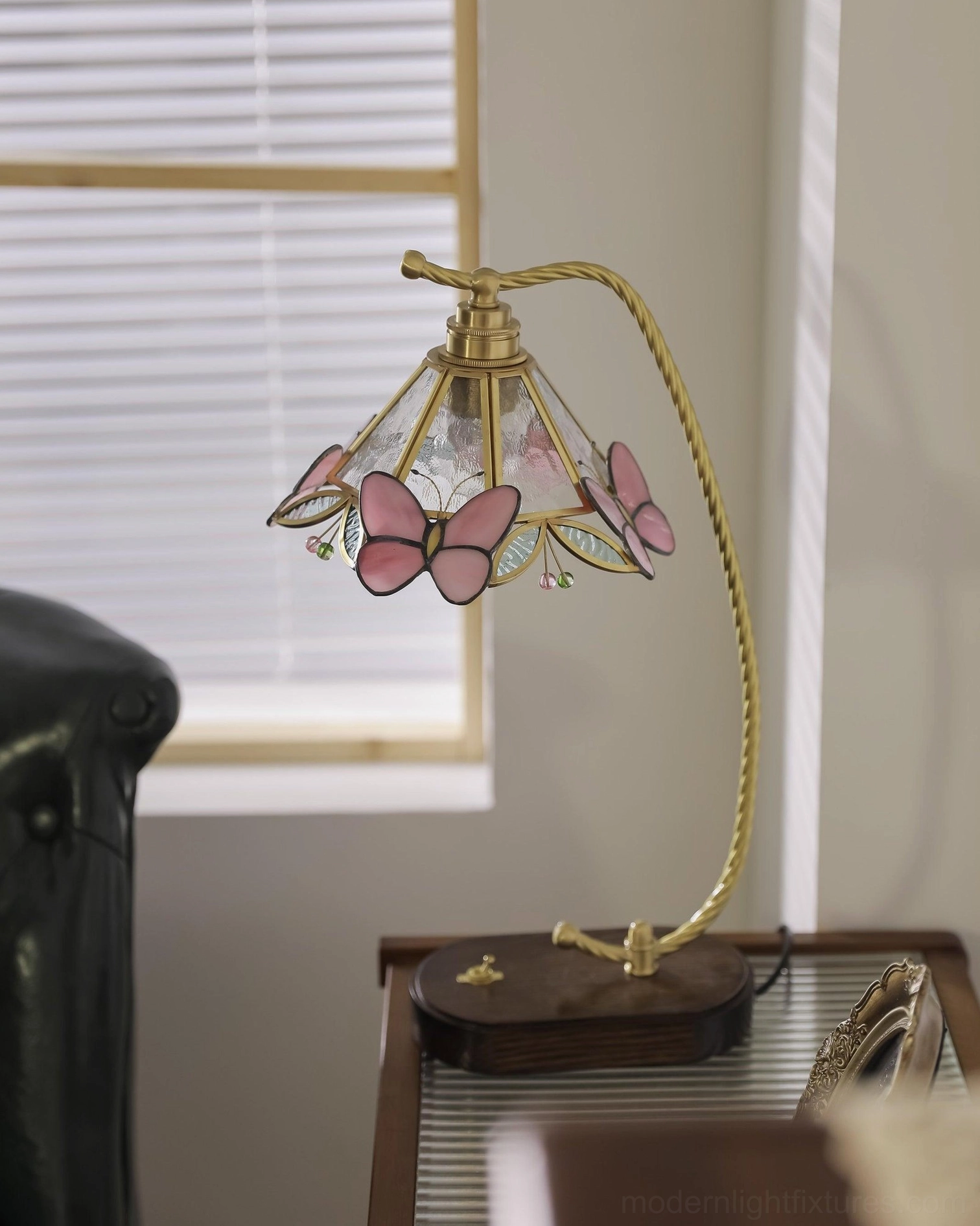 Front three-quarter view of Valerie Butterfly table lamp near louvered window with light purple butterfly trims and curved brass arm detail
