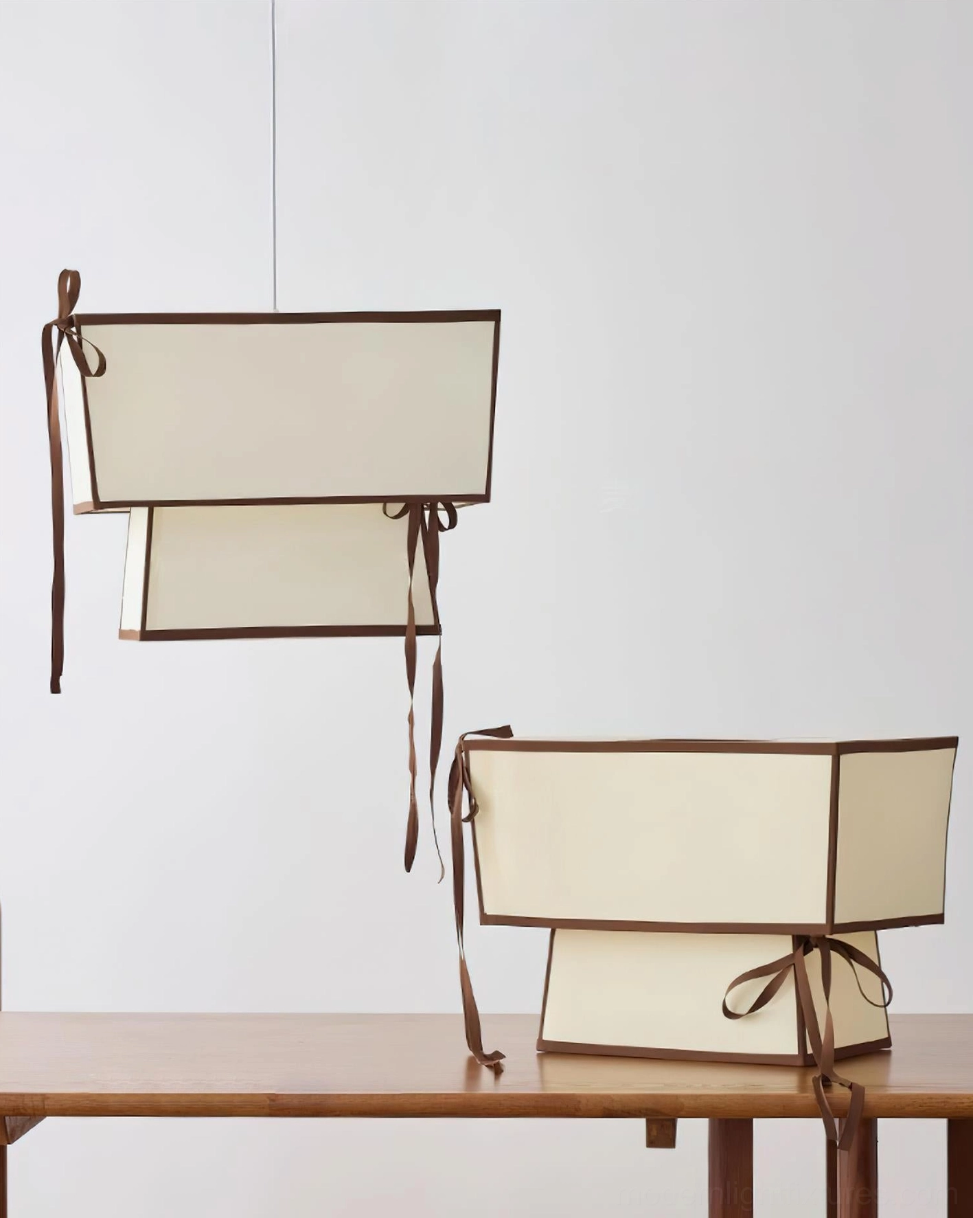 Two Velina fabric pendant lights displayed on wooden surface showing brown ribbon decorations