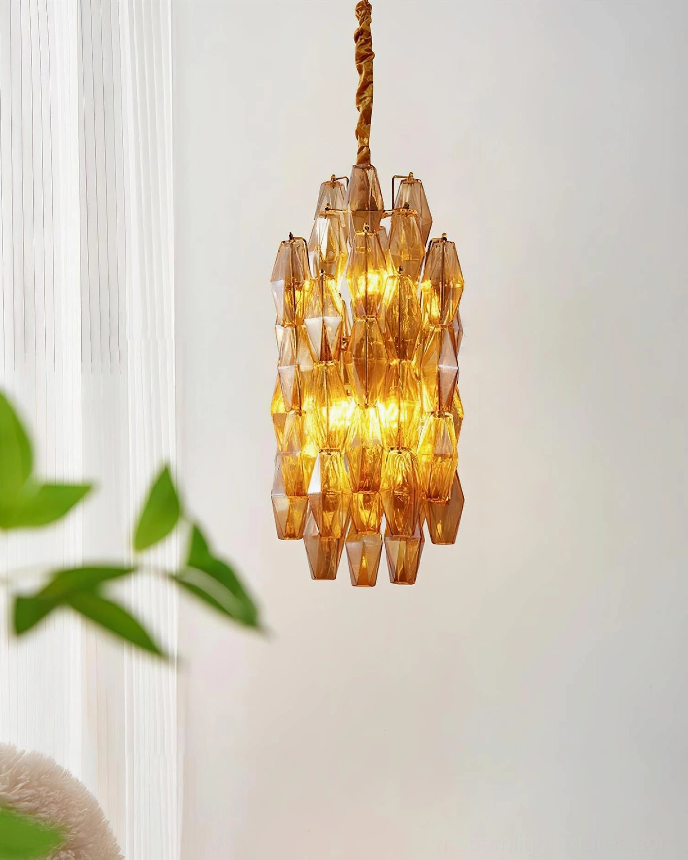 Velthra pendant chandelier with warm amber glass illuminated in modern interior space with white curtains