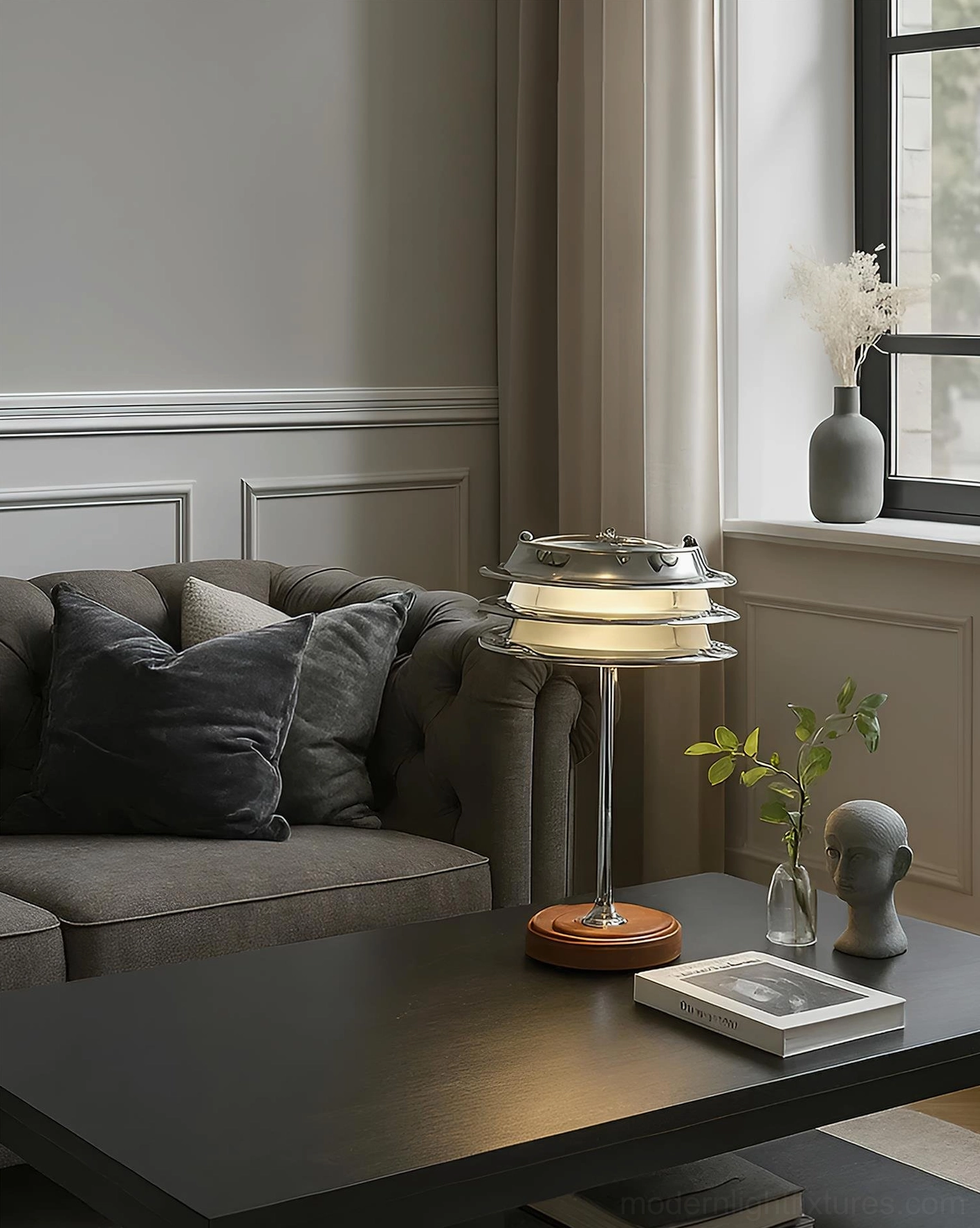 Architectural tiered table lamp placed on dark coffee table with grey sofa in living room