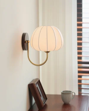 Velum modern wall lamp installed beside bedroom vanity mirror, warm fabric glow, brass curved arm detail