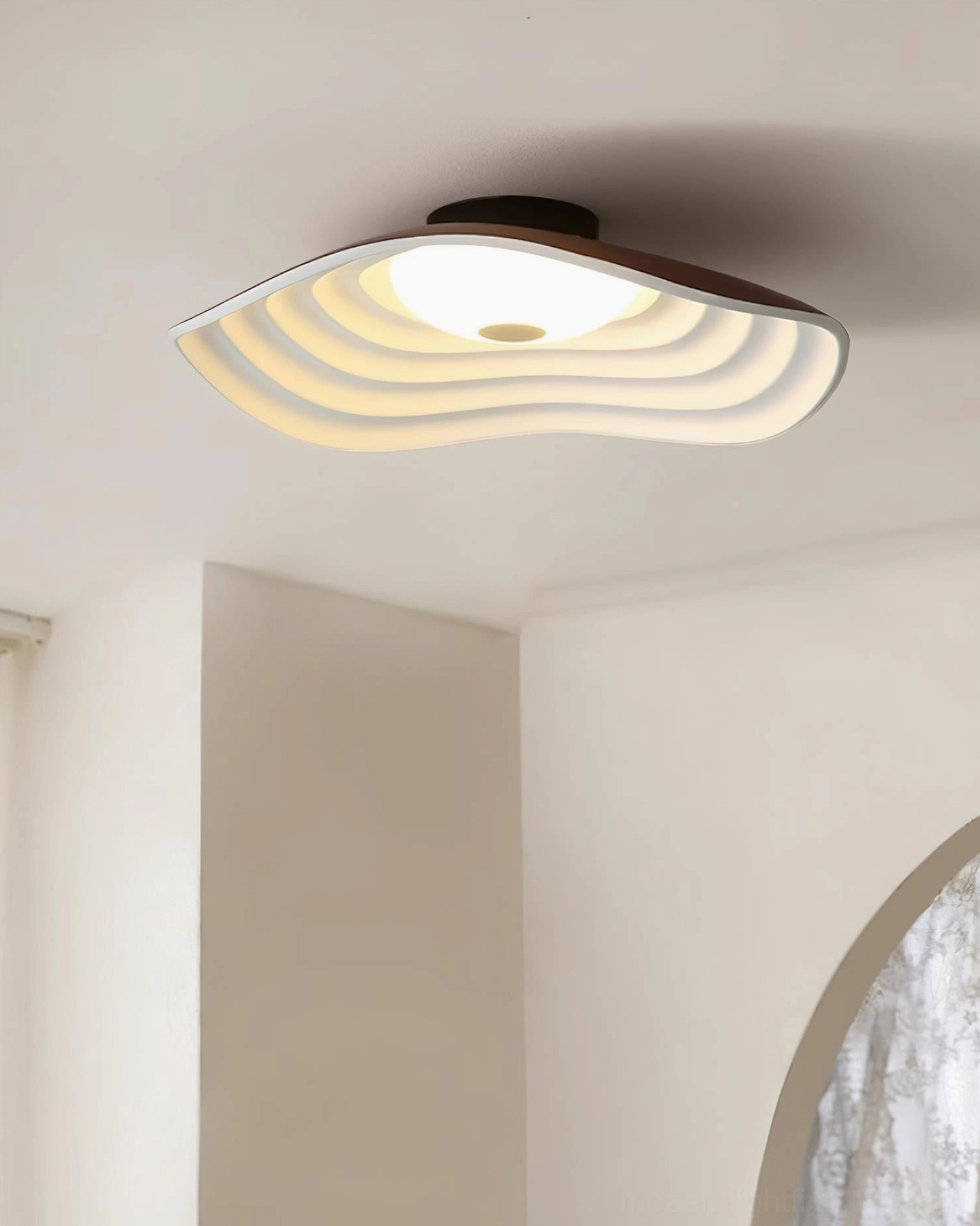 Veneria wavy ceiling light with dark ceiling base and warm glowing wavy shade in minimalist room with arched window detail