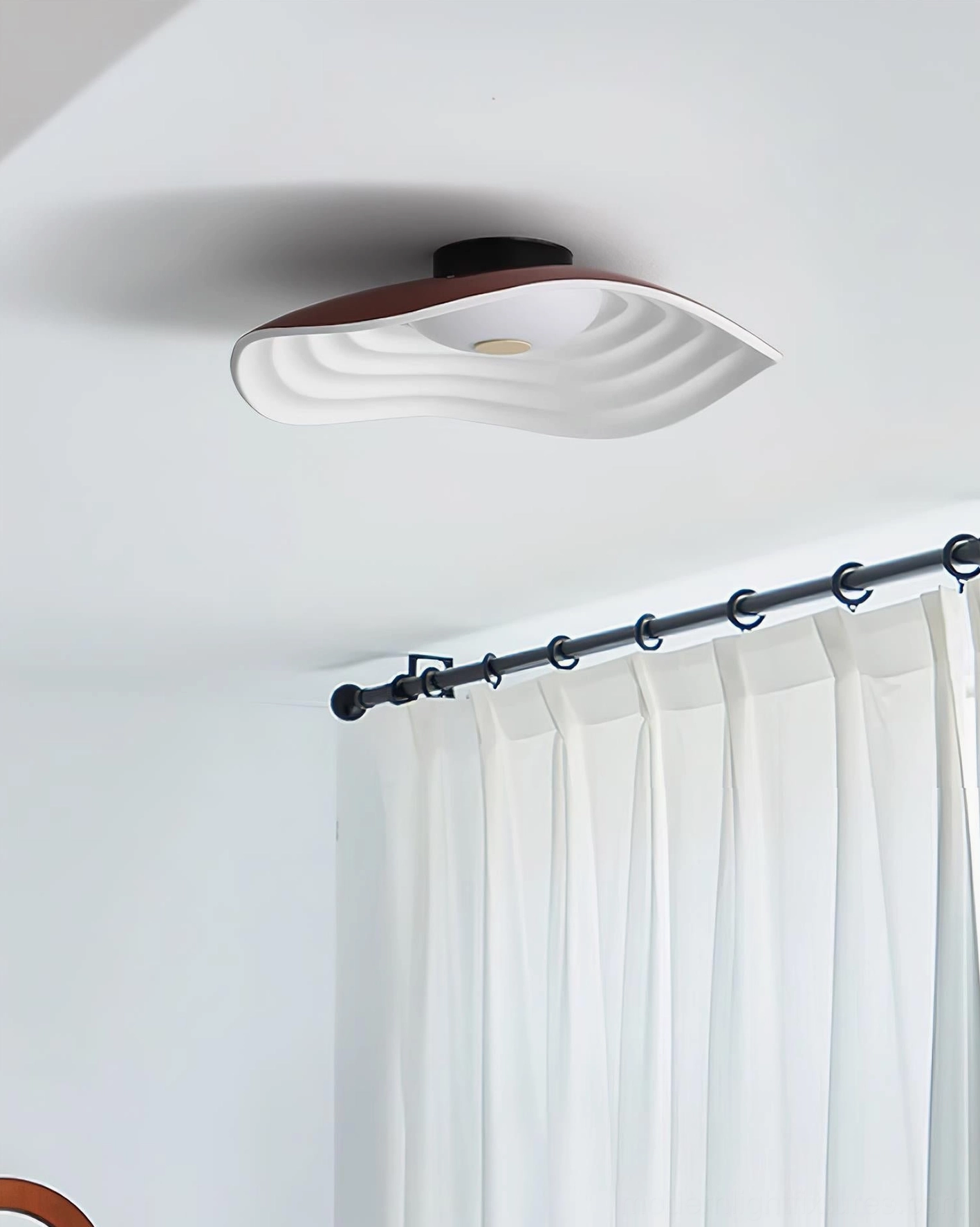 Veneria wavy ceiling light with unlit matte diffuser mounted on ceiling with dark base in minimalist modern room with black curtain rod