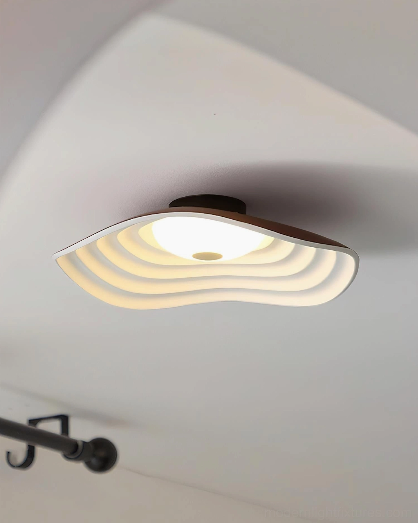 Veneria wavy flush ceiling light with layered warm light diffuser and brown trim mounted on white ceiling with black curtain rod